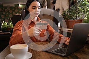 Young cute woman holding credit card and using laptop computer sitting in cafe. Businesswoman working at coffee shop