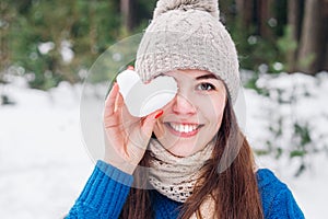 Young cute woman holding snow heart in winter forest. Love concept. Valentine day background.