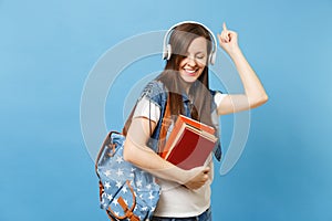 Young cute woman student in denim clothes with backpack headphones listen music hold school book pointing index finger