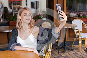 Young cute woman using phone sits in cafe at table with smartphone, answering