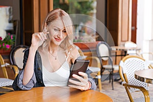 Young cute woman using phone sits in cafe at table with smartphone, answering
