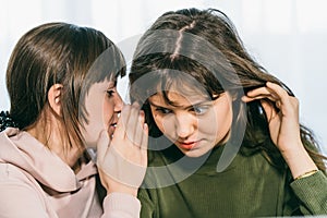 Young cute woman whispering secret on ear to her female friend. Communication and surprised girl by gossip