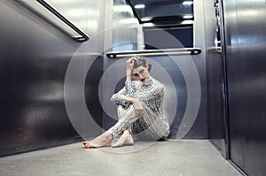 Young cyber woman in silver futuristic costume sitting in the elevator.