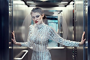 Young cyber woman in silver futuristic costume standing in the elevator.
