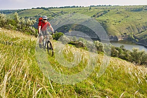 Young cyclist cycling in the green summer meadow against beautiful landscape.