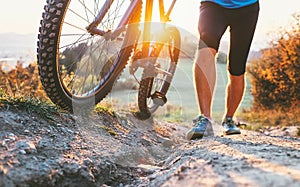 Young cyclist man pushing a mountain bike up the hill close up i