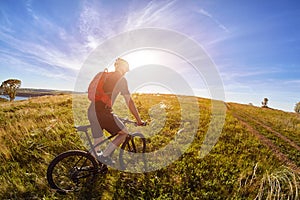 Young cyclist with mountain bicyclist on the path of the field in the countryside against sunrise.