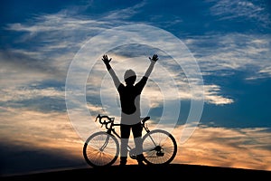 Young cyclist raised hands at sunset sky.