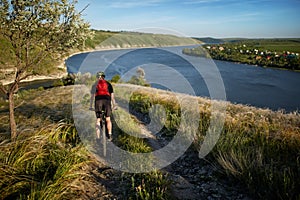 Young cyclist riding mountain bike uphill along a country road above river.