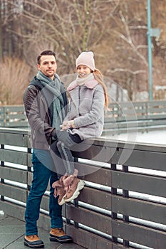 Young dad and adorable little girl have fun on skating rink outdoors