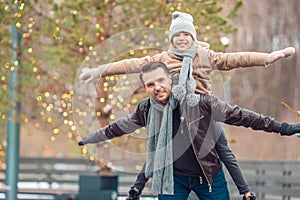 Young dad and adorable little girl have fun on skating rink outdoors