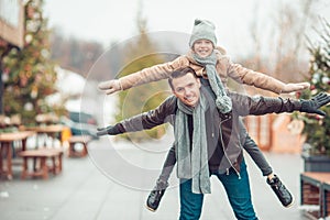 Young dad and adorable little girl have fun on skating rink outdoors