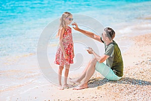 Young dad applying sun cream to daughter nose on the beach. Sun protection