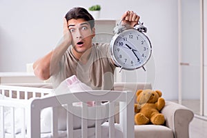 The young dad with clock near newborn baby bed cot