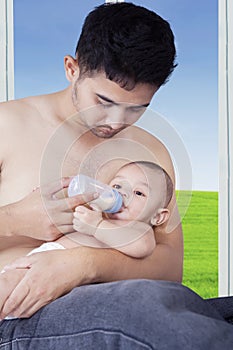 Young dad feeding his baby near the window