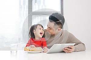 Young dad and his daughter eating pizza and using ipad