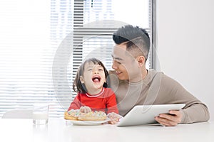 Young dad and his daughter eating pizza and using ipad