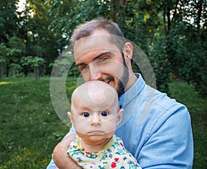 Young dad holding his baby son on the background of a summer landscape. Father is happy and smiling