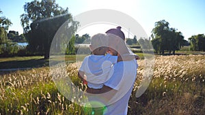 Young dad holding his son on hands at the meadow and talking something to him. Happy family spending time together on a