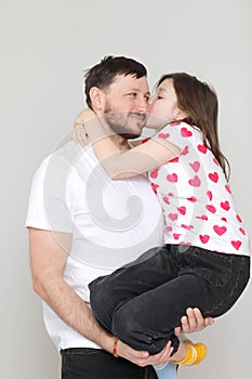 young dad holds his little daughter in his hands. father hugging his child with love and child kiss him. man in white t