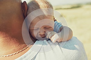 Young dad holds a newborn baby on his shoulder, walking in nature. happy father is wearing shorts and a t-shirt. International