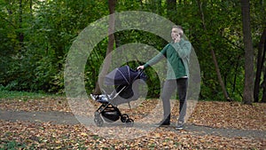 A young dad is talking on the phone and rocking his child in a stroller. A man speaks on the phone in the autumn forest.
