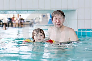 Young dad teaching his little son to swim indoors