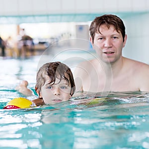Young dad teaching his little son to swim indoors