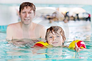 Young dad teaching his little son to swim indoors