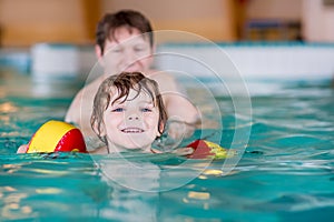 Young dad teaching his little son to swim indoors