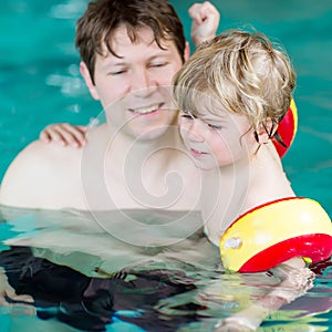 Young dad teaching his little son to swim indoors