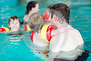 Young dad teaching his two little sons to swim indoors