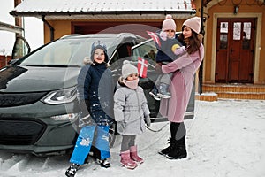 Young dannish mother with kids hold Denmark flags and charging electric car in the yard of her house at winter
