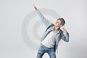 Young dark-haired guy with black backpack on his shoulder dressed in a white t-shirt, jeans and a denim jacket raised