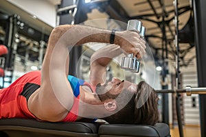 Young dark-haired man in bright tshirt working on his body in gym