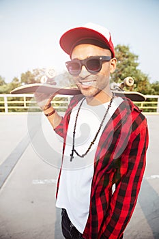 Young dark skinned guy wearing sunglasses holding skateboard