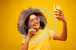 Young dark skinned happy mulatto woman with Afro hairstyle, holds modern mobile phone in front of face