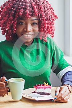 Young dark-skinned woman dressed in clothes holding cup of hot drink, enjoying coffee or tea. Black student girl spending