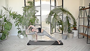 Young darkhair woman practicing yoga in the morning at her home near plants. The woman is engaged in self-determination