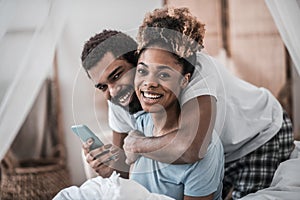 Young darkskinned husband and wife in pajamas with smartphone