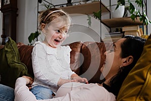 Young daughter and mother playing on the couch together, funny faces