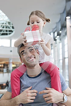 Young daughter sits on fathers shoulders and gives him a present