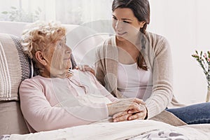 Young daughter supporting sick mother lying in hospital bed