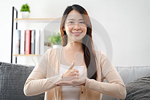 A young deaf woman is sitting on a couch and making a sign Language to communicate