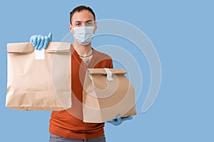 Young delivery man in medical mask holding and carrying a cardbox isolated on blue background. Buy food online in