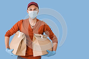 Young delivery man in medical mask holding and carrying a cardbox isolated on blue background. Buy food online in