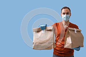 Young delivery man in medical mask holding and carrying a cardbox isolated on blue background. Buy food online in