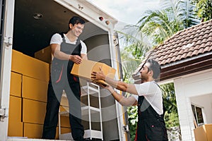 Young delivery men unload boxes from a van. Movers in uniform work together