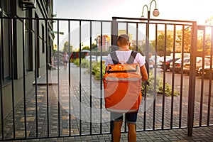 Young deliveryboy walking with red thermal bag on city street. Man of delivery service in hurry to deliver an order.