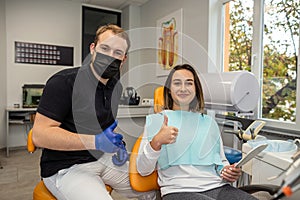 Young dentist doctor and female patient showing thumbs up.